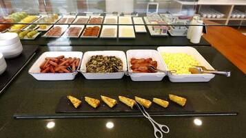 Un bufé con diversas opciones de comida, incluyendo perros calientes, champiñones, tocino y huevos revueltos.