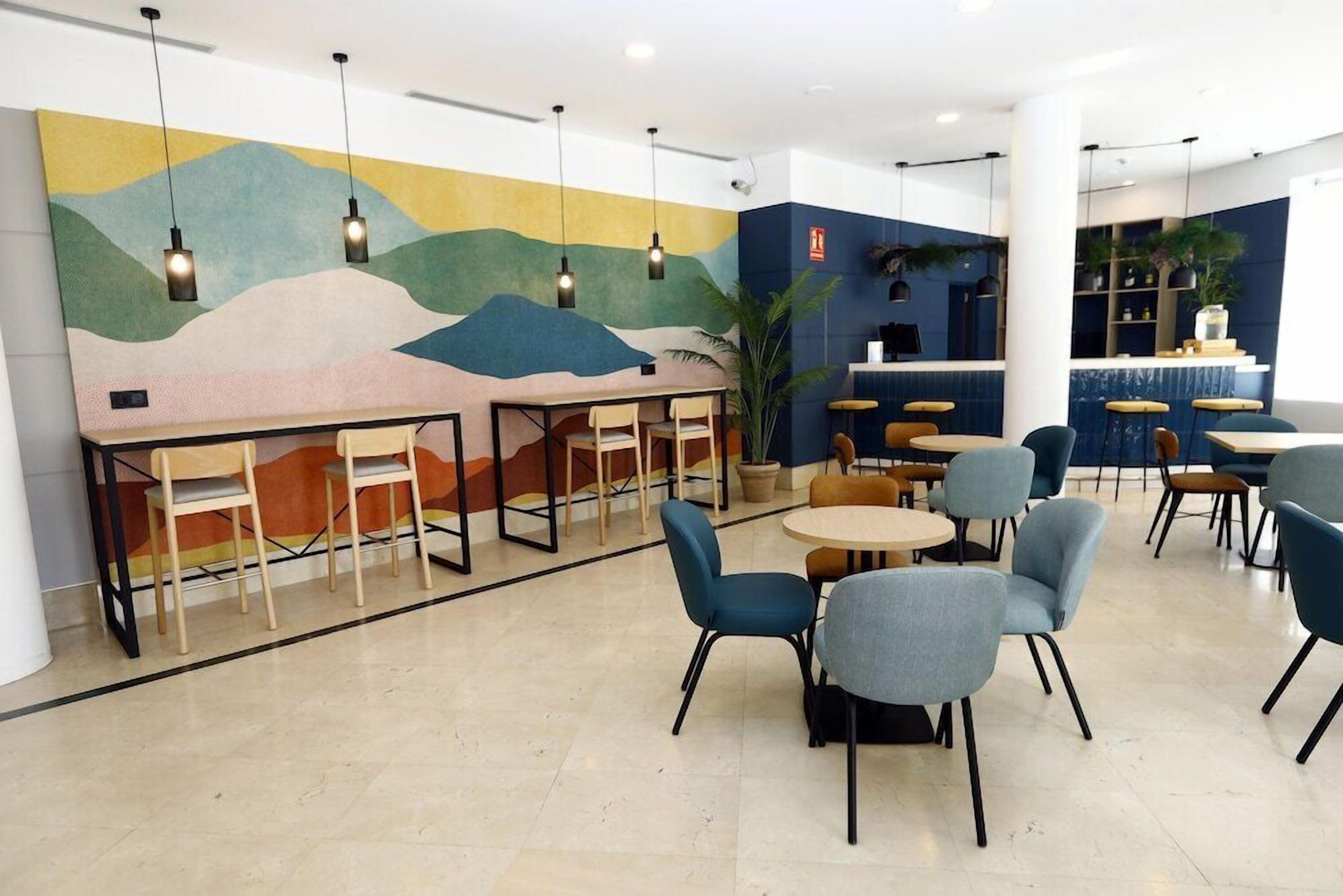 A modern cafe with a mural, round tables, and blue chairs.