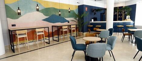 A modern cafe with a mural, round tables, and blue chairs.