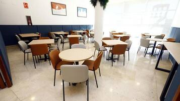 A dining area with round tables and chairs, a white pillar, and framed pictures on the wall.