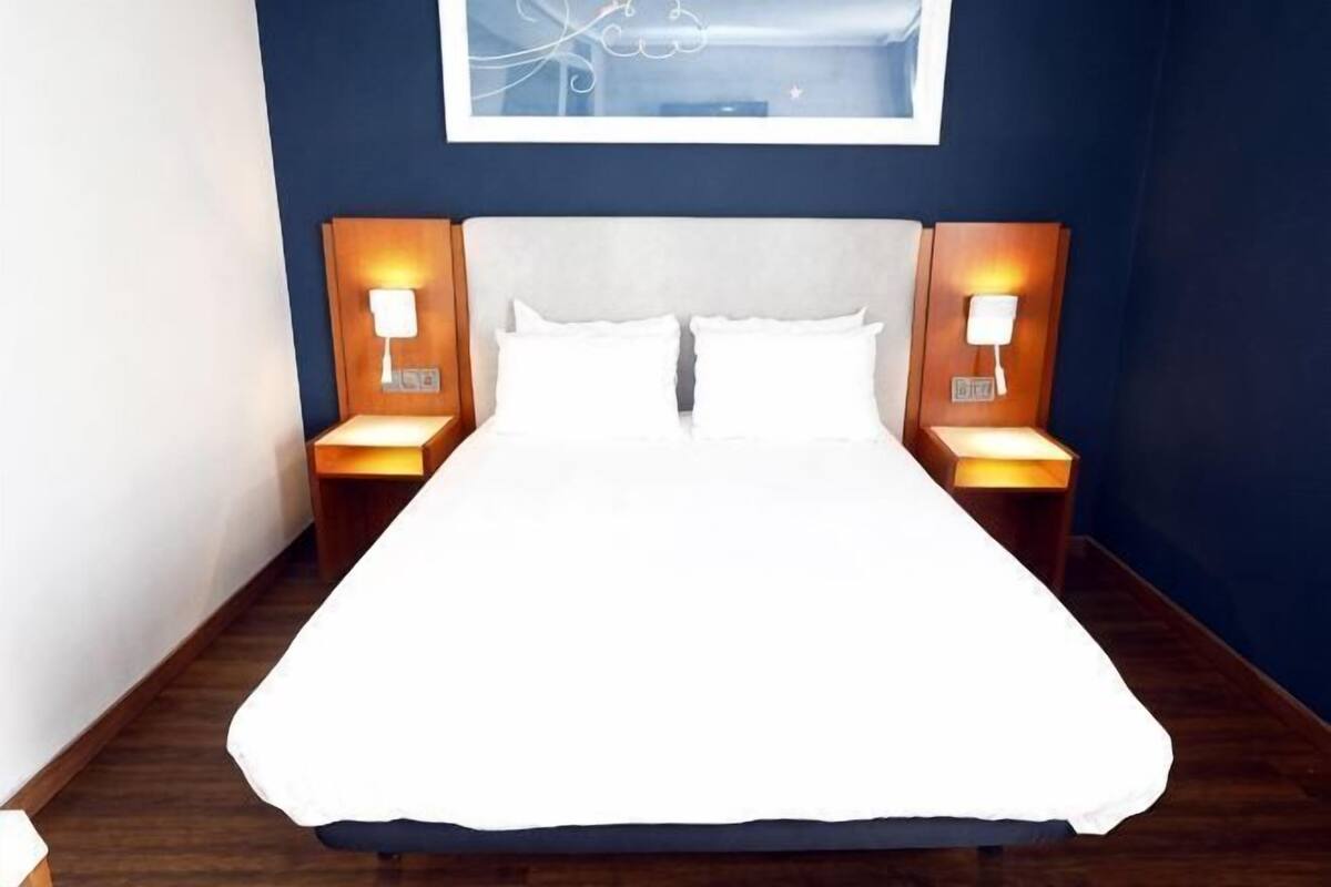 A neatly made bed with white linens, two bedside lamps, and a framed artwork above the bed.