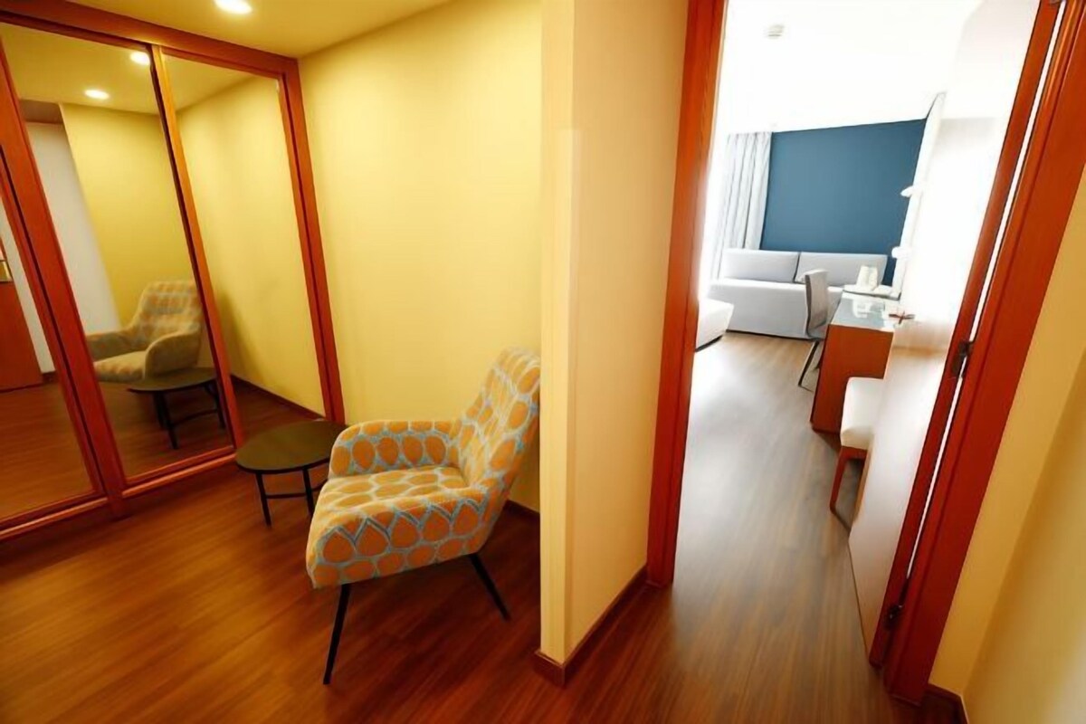Una habitación con suelo de madera, un sillón estampado, una mesita y un espejo.
