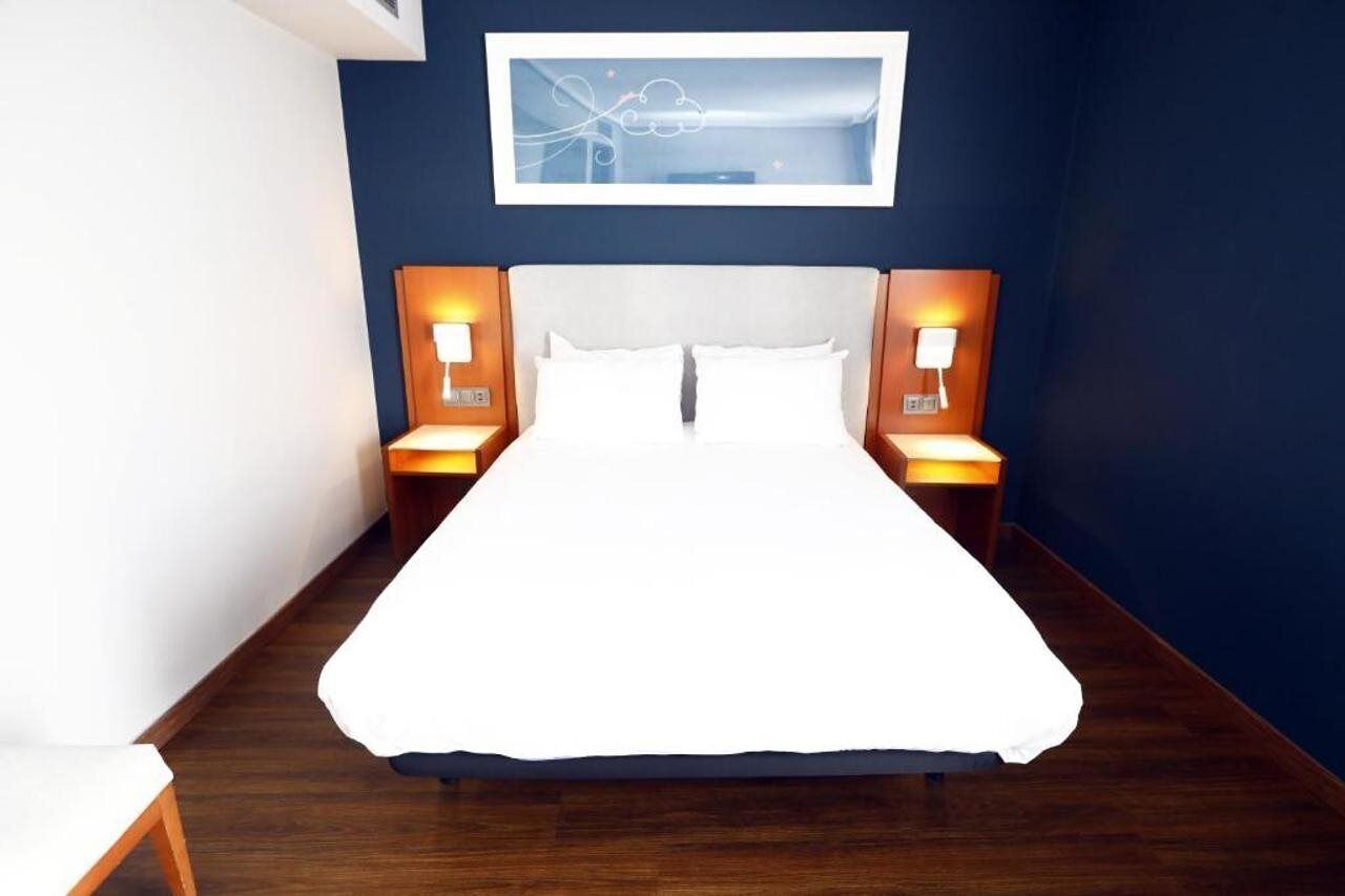 A neatly made bed with white linens, two bedside lamps, and a framed artwork on the wall.