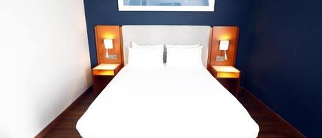 A neatly made bed with white linens, two bedside lamps, and a framed artwork on the wall.