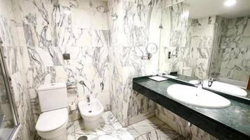 Une salle de bain avec des murs en marbre, des toilettes, un bidet, deux lavabos et un grand miroir.