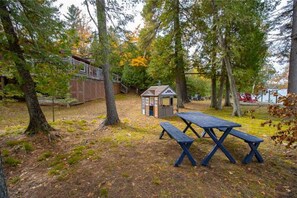 Een picknickplaats met een houten tafel en banken, omringd door bomen en een klein, hutachtige gebouw.