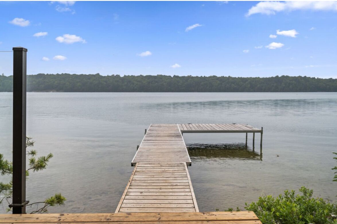 A wooden dock extending into calm water with a forested shoreline in the background.