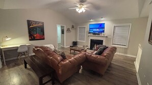 A living room with two brown leather sofas, a wooden coffee table, a TV on a mantel, and a desk with a lamp. - The Lodge @ Greens Mill - 30% discount for 28+ days (Spring Hill)