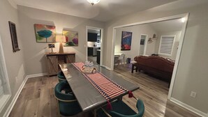 A dining area with a long table, teal chairs, and a red and white striped table runner. There is a small wooden cabinet with a lamp, and a painting on the wall. - The Lodge @ Greens Mill - 30% discount for 28+ days (Spring Hill)