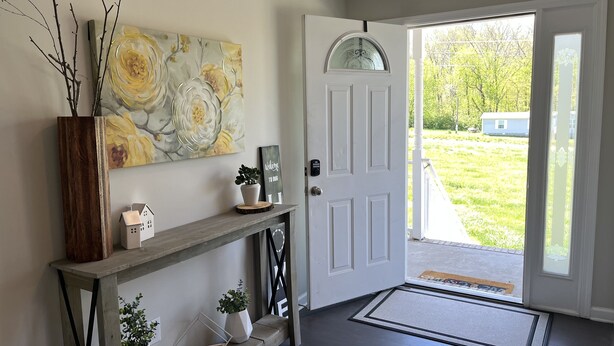A hallway with a wooden console table, a welcome sign, a potted plant, and a door leading to a yard. - The Lodge @ Greens Mill - 30% discount for 28+ days (Spring Hill)