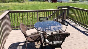 A wooden deck with a glass table and wicker chairs, overlooking a grassy area with a barn and trees. - The Lodge @ Greens Mill - 30% discount for 28+ days (Spring Hill)