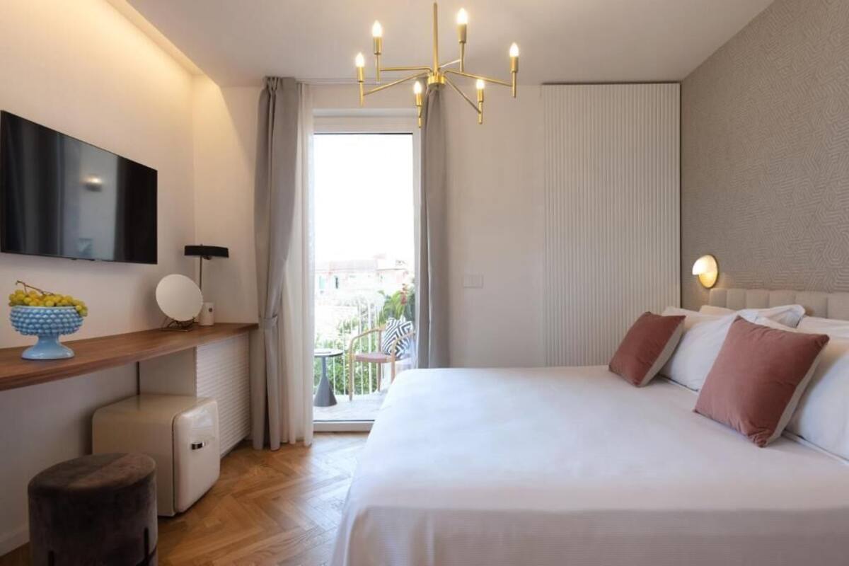 Una habitación de hotel moderna con una cama grande, un televisor de pantalla plana, una mesita con un frutero, una silla y un balcón con vistas.