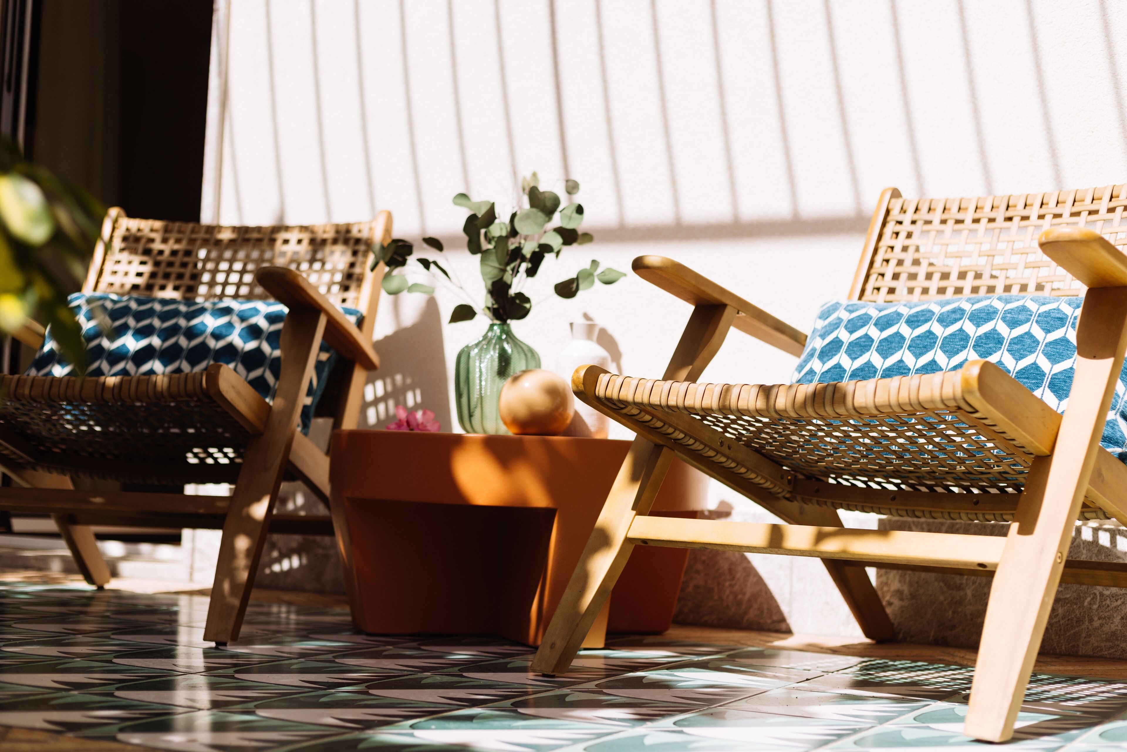 Dos sillones de mimbre con cojines estampados, una planta en maceta y un suelo de baldosas.