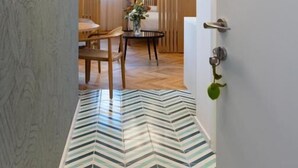 Un pasillo de diseño moderno, con un suelo de patrón en zigzag, una puerta de madera y un comedor con mesa y sillas.