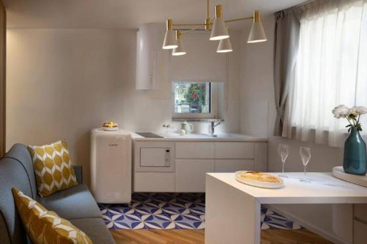 Habitación de hotel moderna con sofá, mesa de comedor, pequeña cocina y ventana con cortinas.