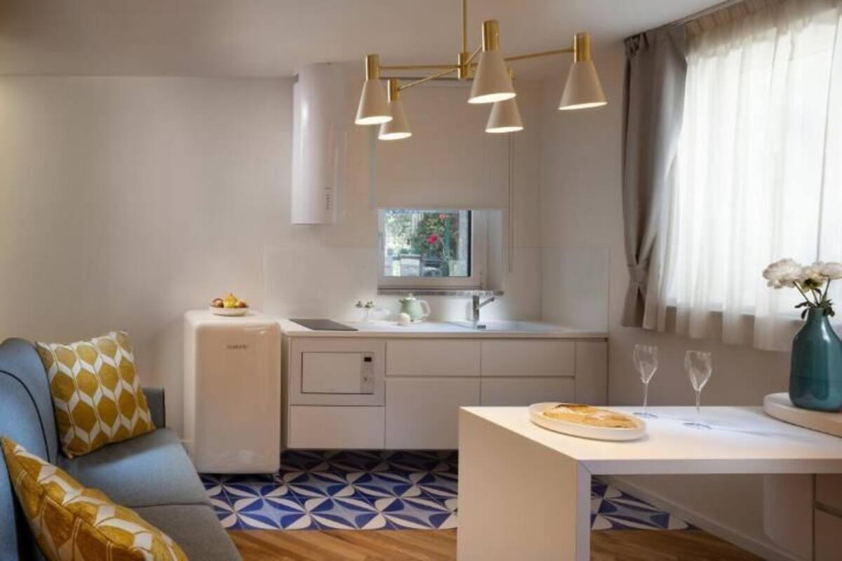 Una kitchenette compacta con horno integrado, un refrigerador pequeño y un comedor con una mesa y sillas blancas.