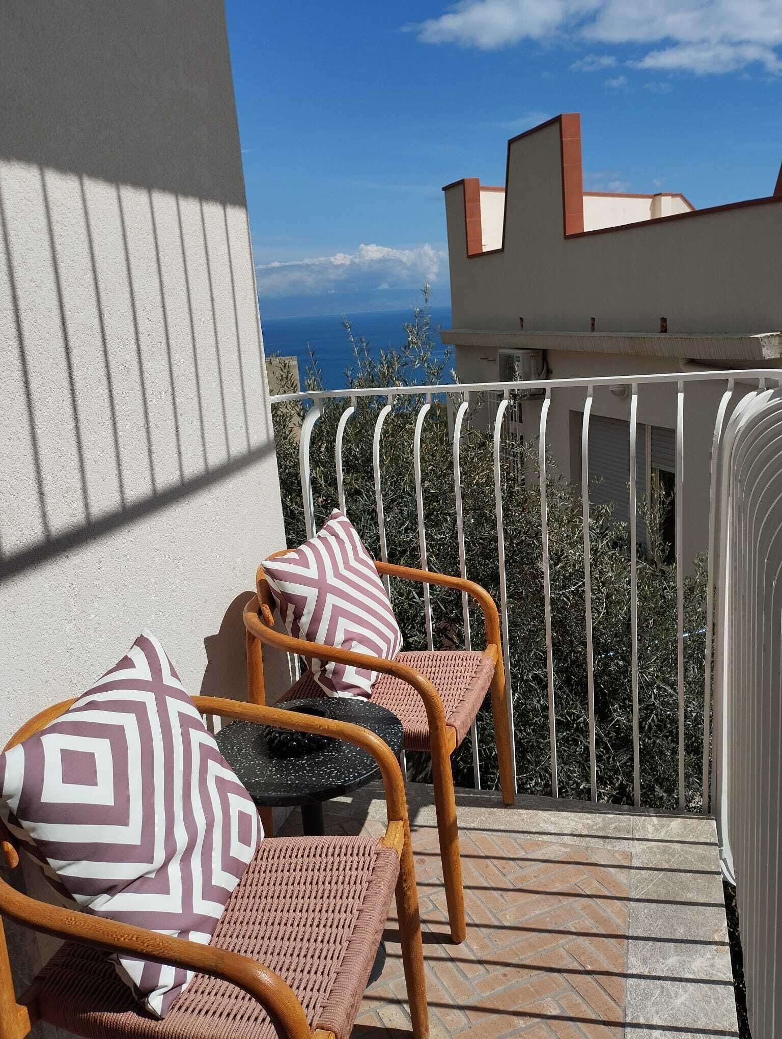 Ein Balkon mit zwei Korbstühlen, einer mit gemustertem Sitzkissen und der andere mit einfarbigem Sitzkissen.