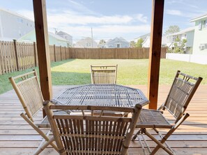 Een houten terras met een tafel en stoelen, een houten omheining en huizen op de achtergrond.