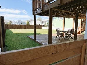 Een houten terras met een tafel en stoelen, een gazon en een houten omheining.