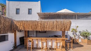 A wooden deck with a bar area, a thatched roof, and a white building with windows. - Costa Viva Bodrum (Bodrum)