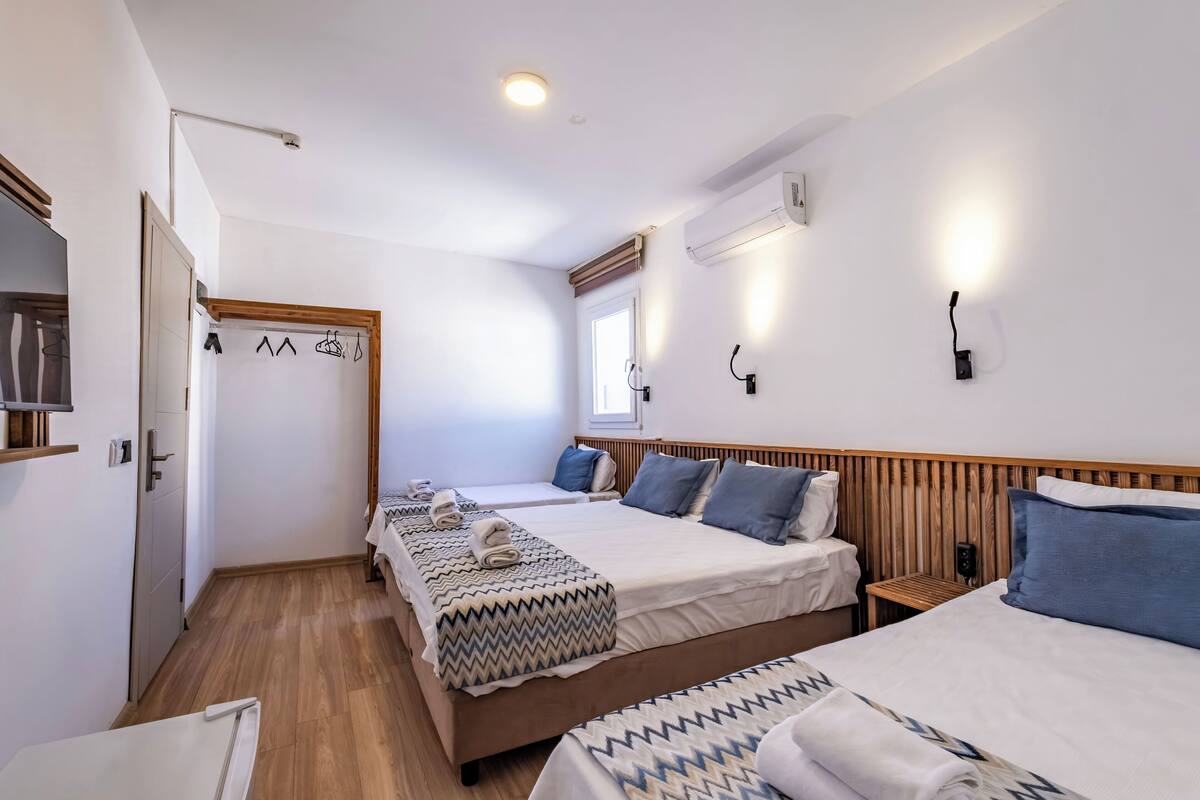 Habitación de hotel con dos camas, piso de madera, pared blanca y una ventana.