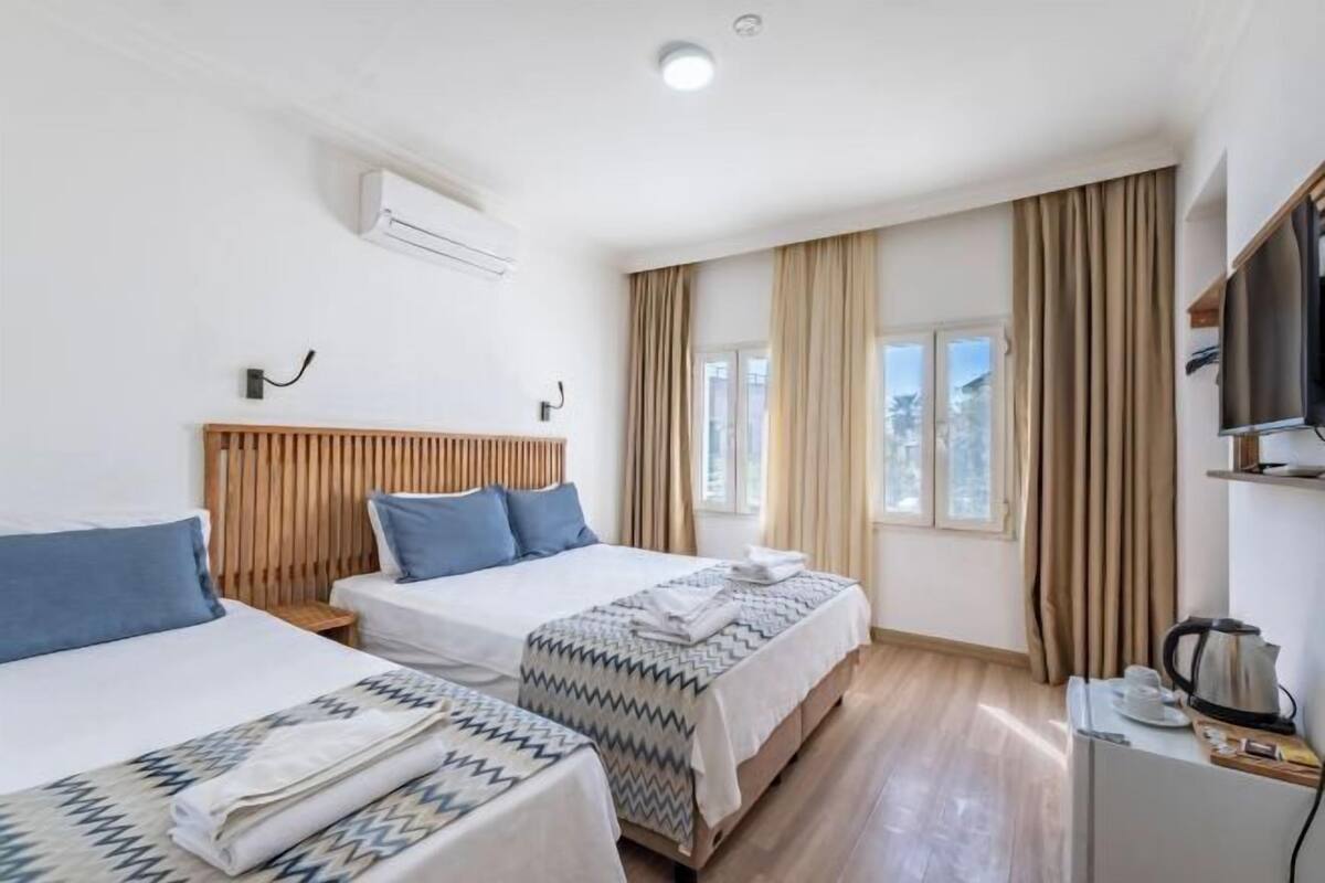 Habitación de hotel con dos camas, televisión, tetera y ventana con cortinas.