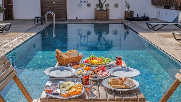 A poolside dining setup with various food items and drinks, a wooden deck, and a thatched roof structure. - Costa Viva Bodrum (Bodrum)