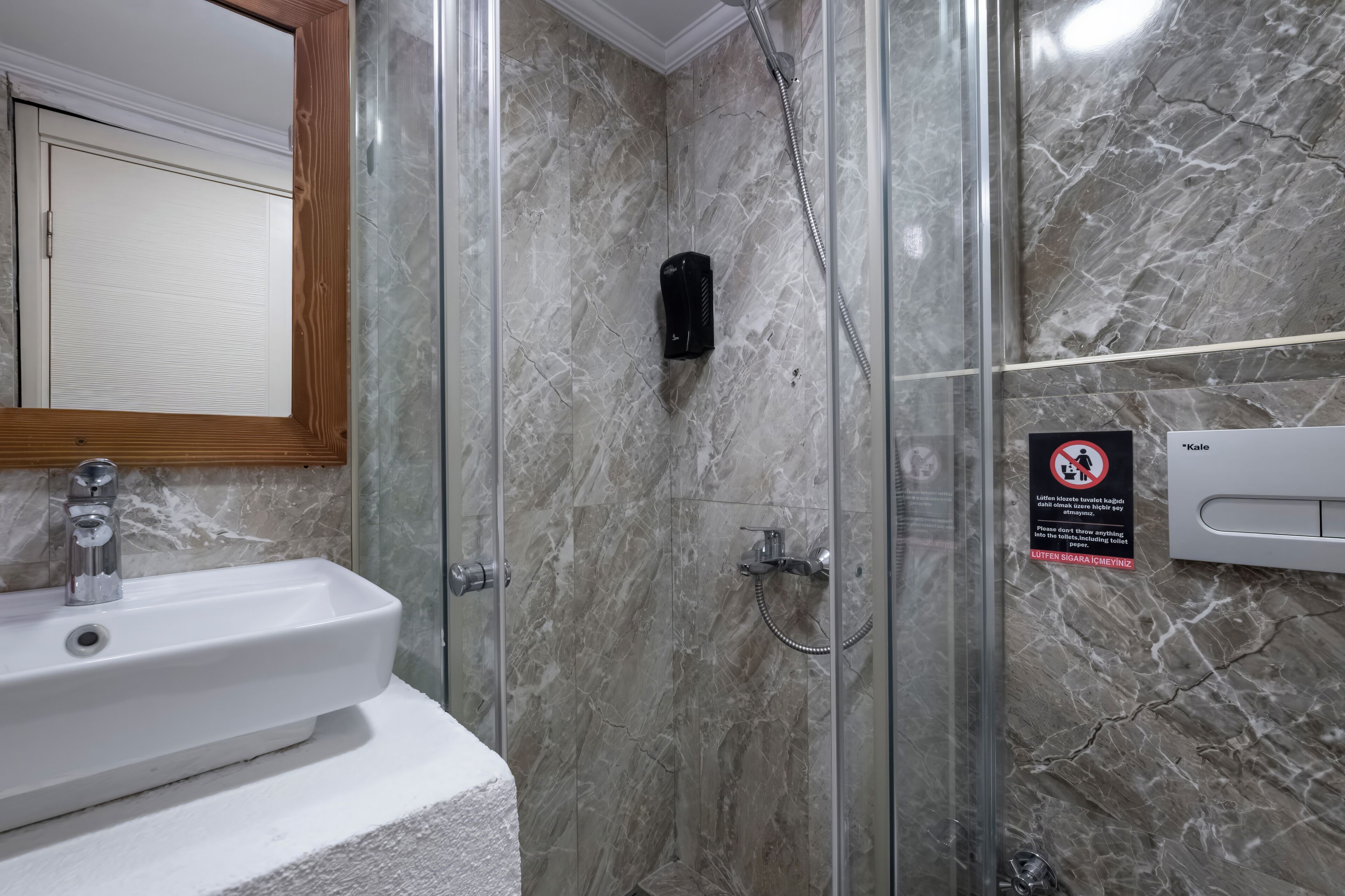 A bathroom with a marble wall, a sink, a glass shower enclosure, and a no-smoking sign.
