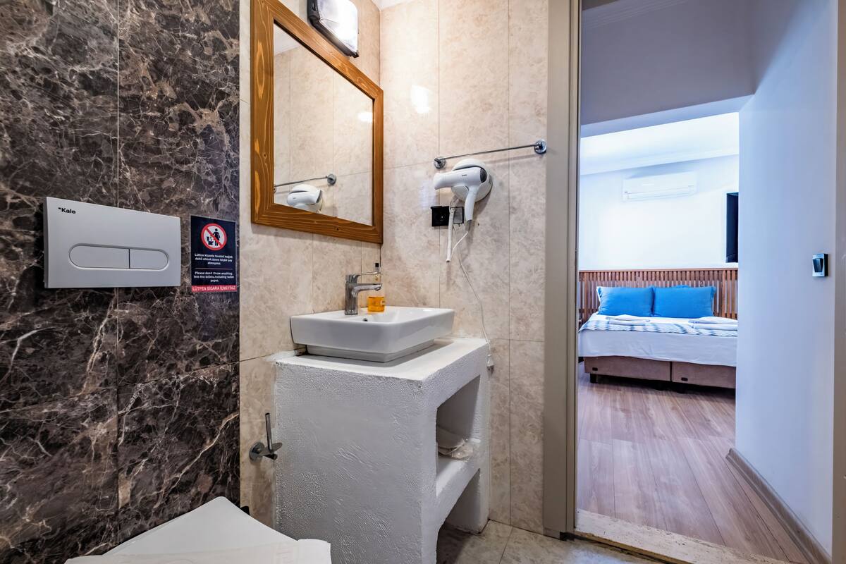 Un baño con pared de mármol, un lavamanos blanco, un espejo y un secador de pelo en un soporte de pared.