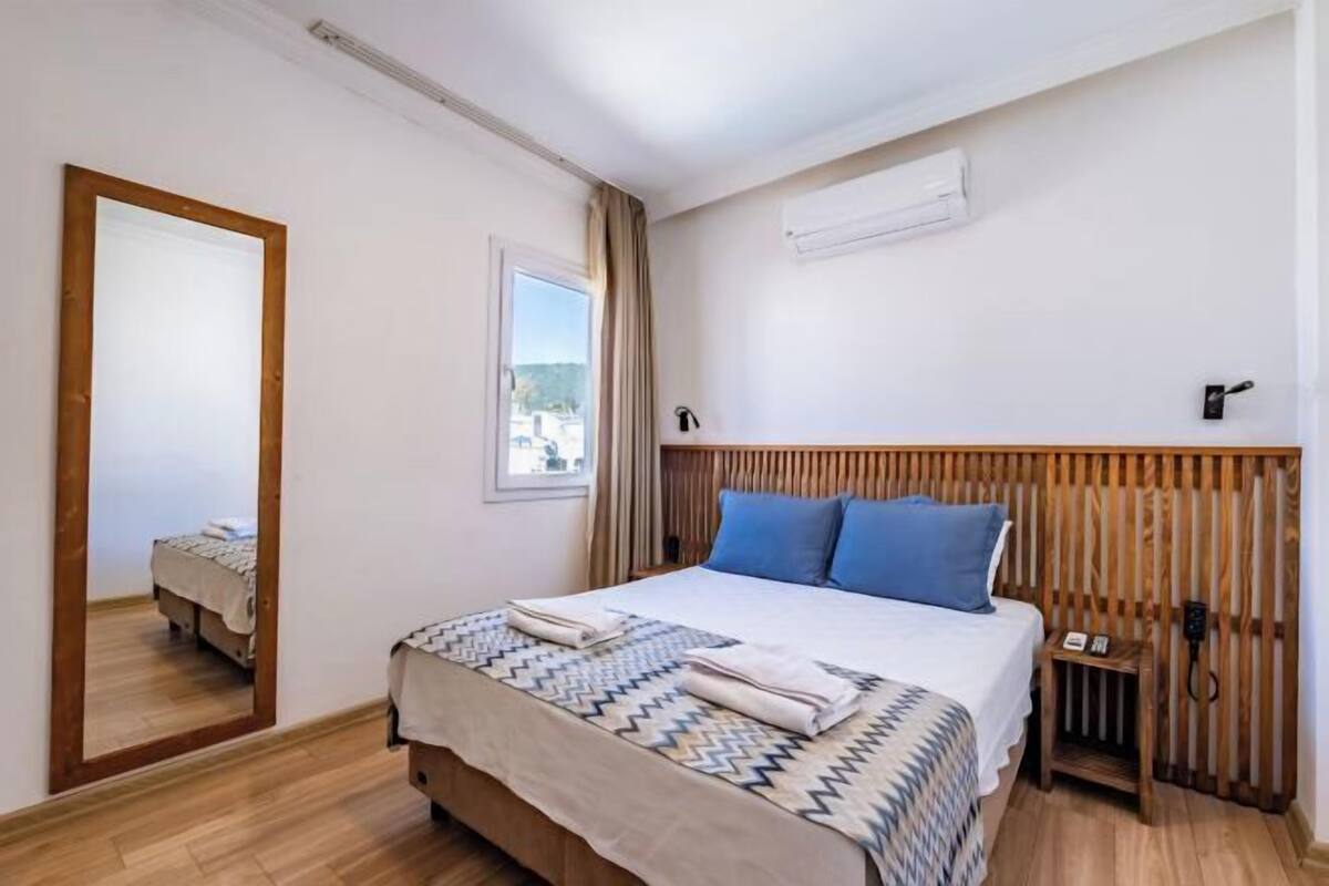 Un dormitorio con cama, mesita de noche, espejo y ventana.