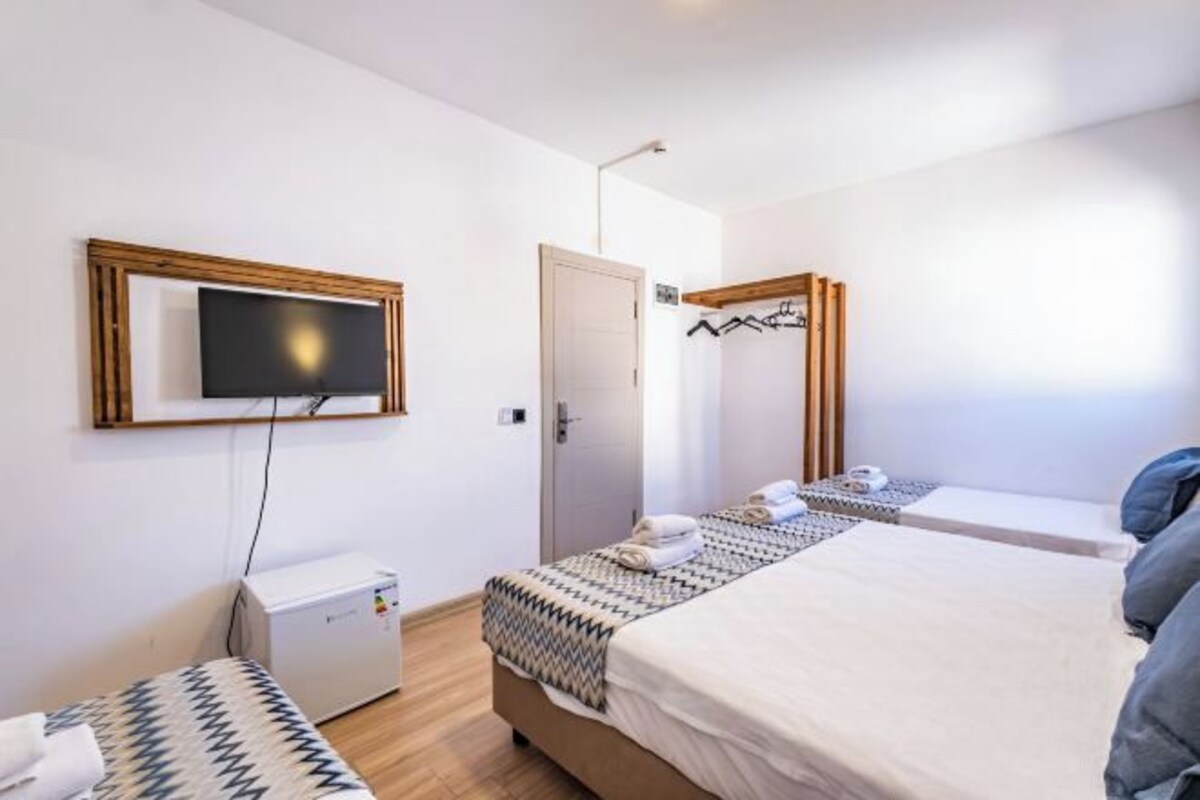 A hotel room with a bed, a TV mounted on the wall, a small desk, and a door.