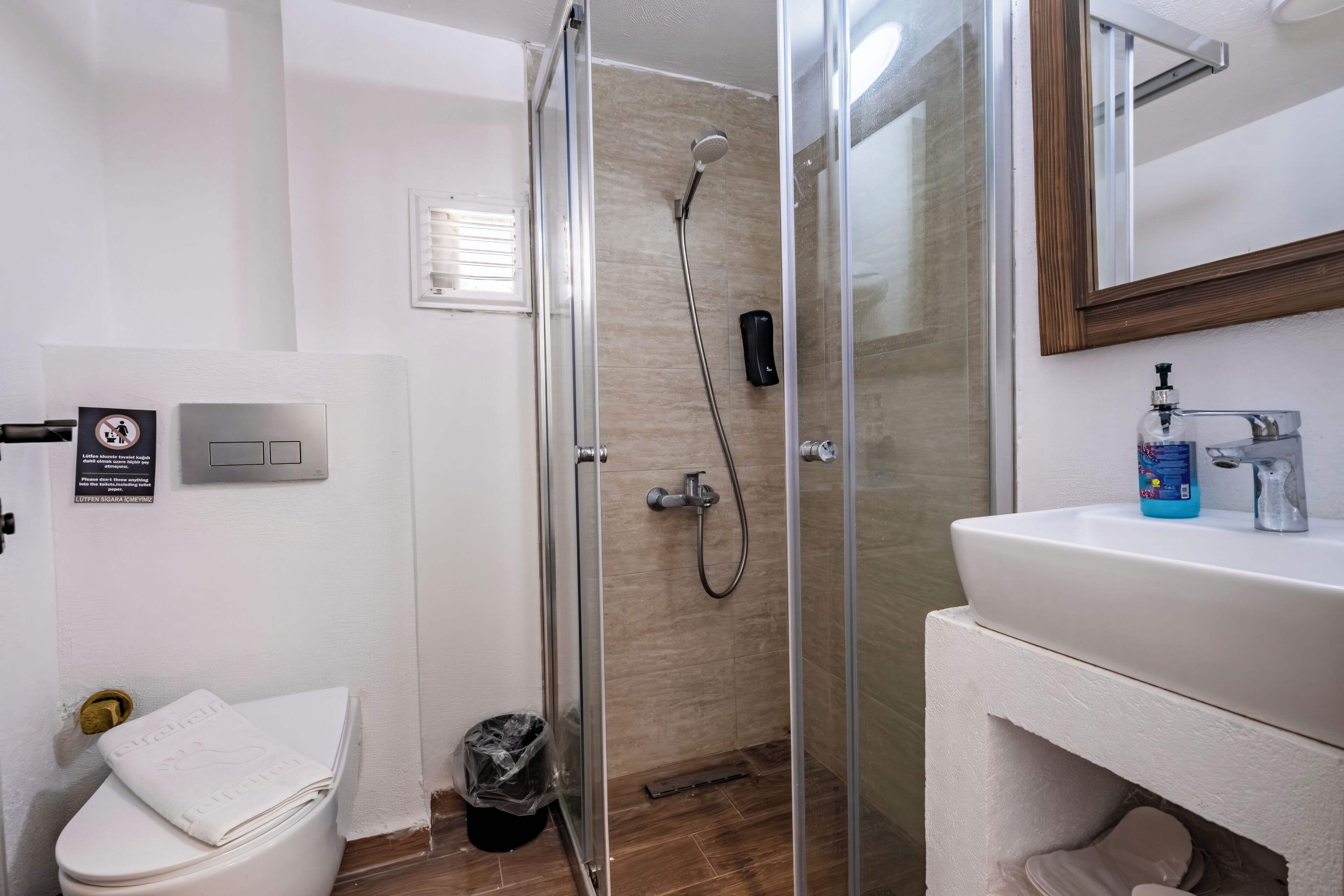 A bathroom with a glass-enclosed shower, a white sink with a mirror, and a toilet with a towel on it.