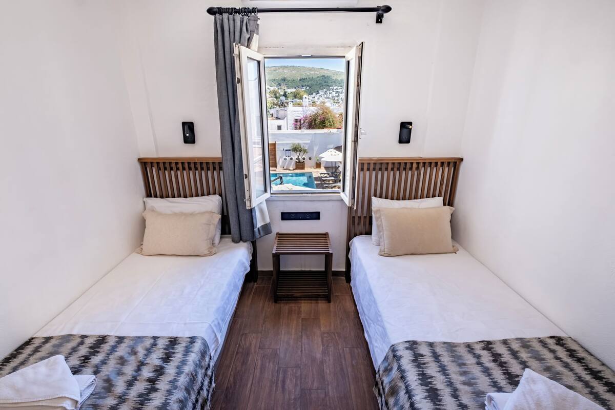 Una habitación con dos camas, una mesita y una ventana que da a una piscina y edificios.
