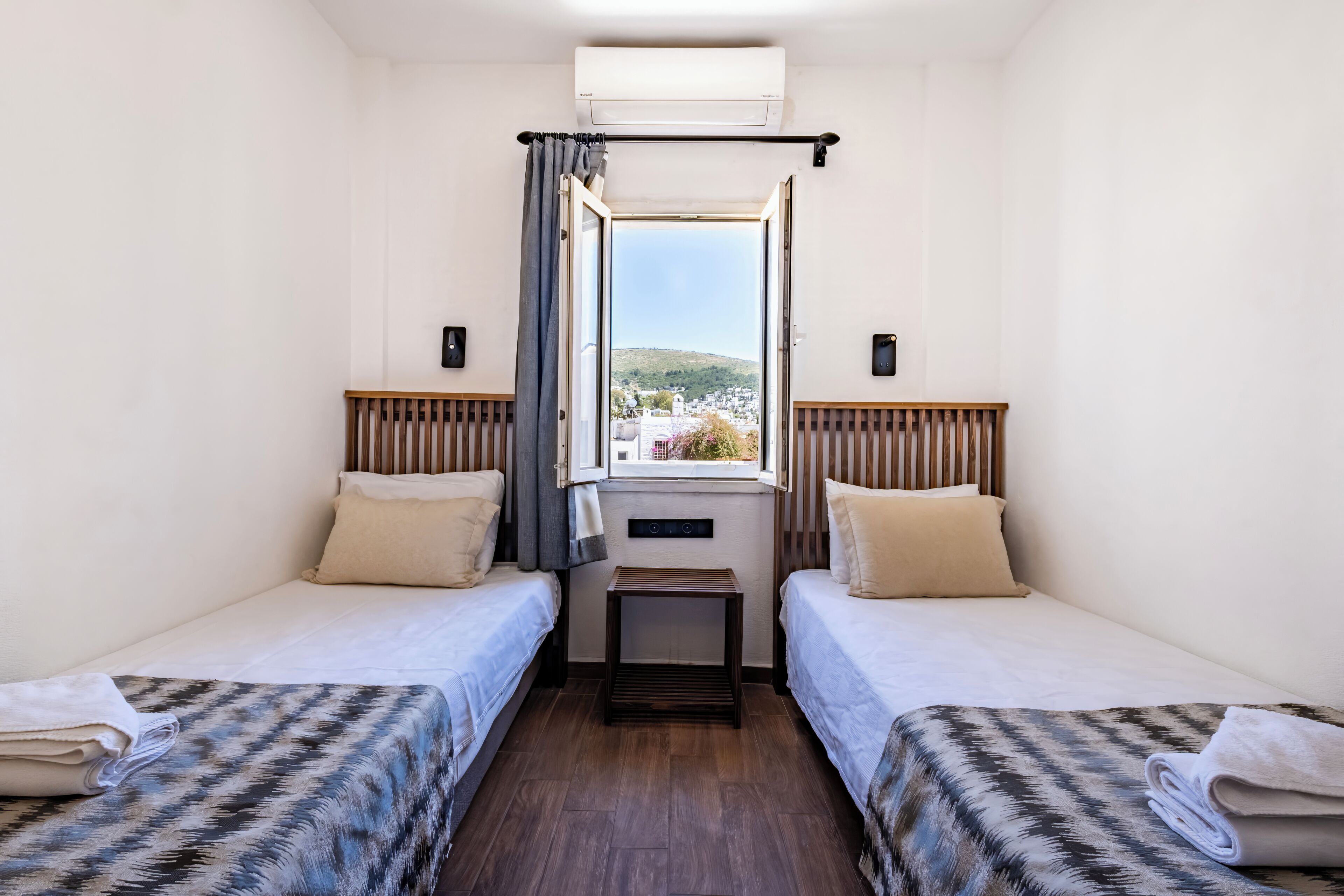 A room with two beds, a small table, and a window with a view.