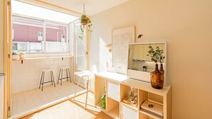 Cocina moderna con un amplio ventanal, taburetes blancos, encimera blanca y un armario de madera con espejo y un jarrón.