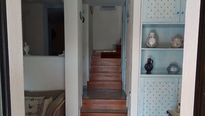 A staircase leading to a second floor, a wicker sofa with cushions, and a cabinet with decorative items. - Apartment in a residential complex 5 minutes from Campulongu Beach (Villasimius)