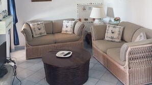A living room with two sofas, a round coffee table, and a lamp. There are framed pictures on the wall and a small shelf with decorative items. - Apartment in a residential complex 5 minutes from Campulongu Beach (Villasimius)