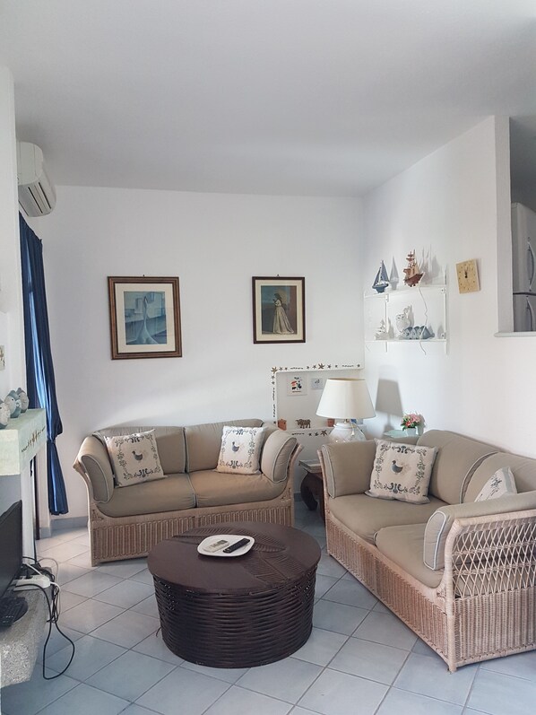 Un saló amb dos sofàs, una taula rodona de centre i una làmpada. A la paret hi ha fotografies emmarcades i una petita estant amb objectes decoratius.