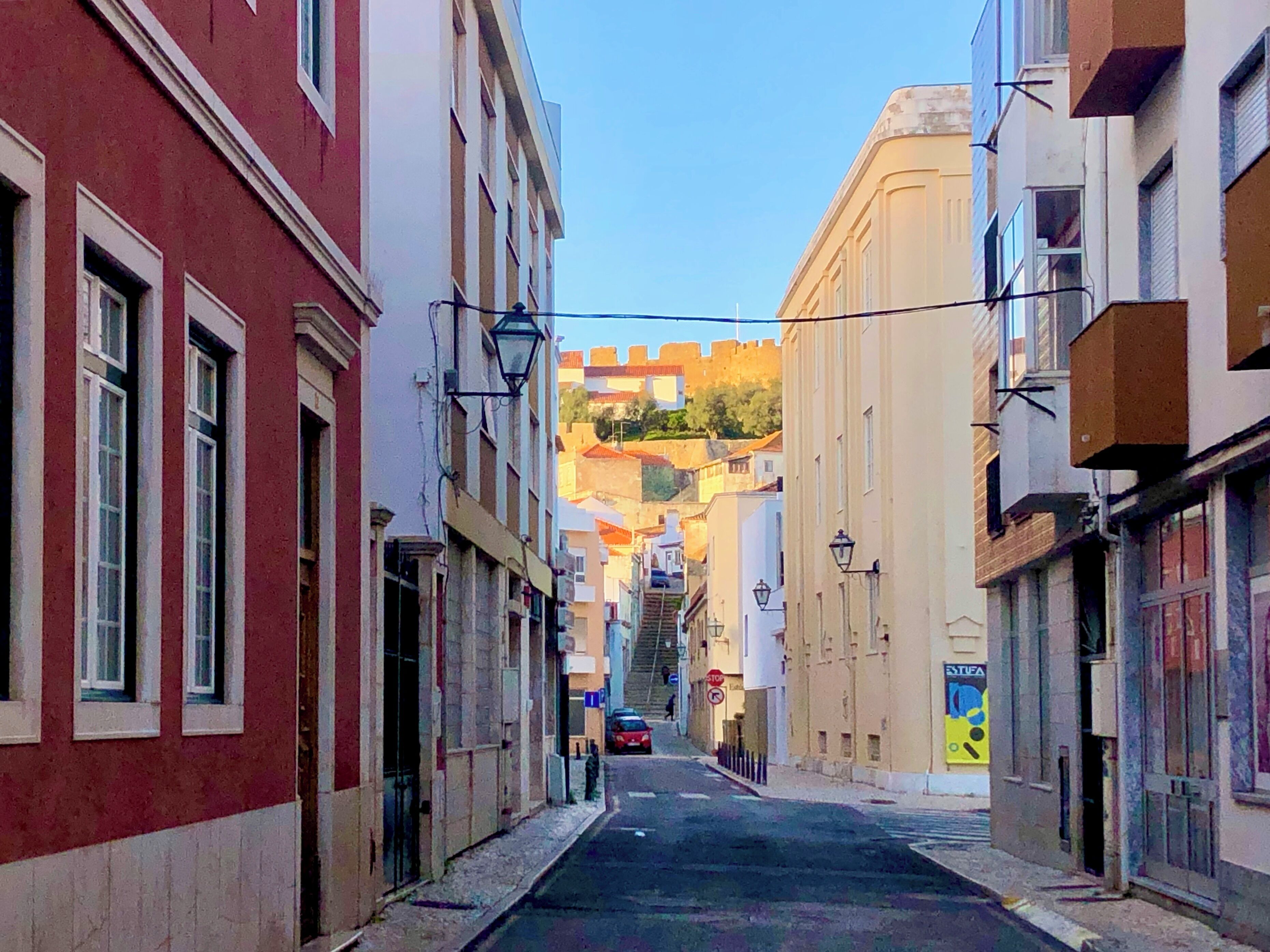 A narrow street with buildings on either side, a visible stop sign, and a car parked on the street.
