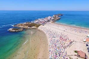 Ett flygbildsbild av en strand med en klippig kustlinje, ett sandigt strandområde och en samling färgglada parasoller.