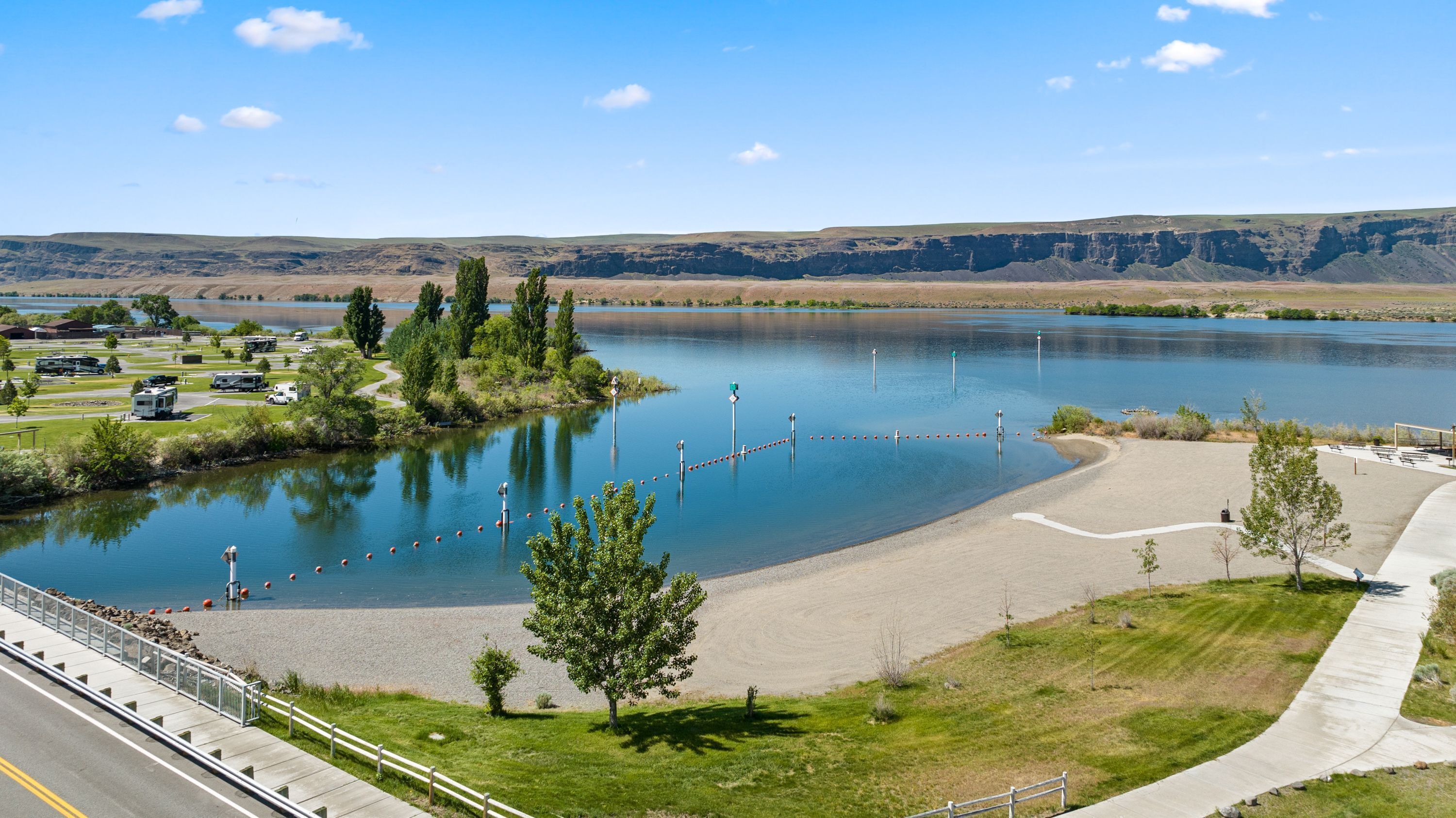 A lakeside view with a parking area, RVs, and a walking path.