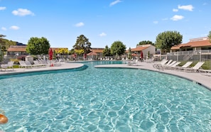 Una piscina amplia y despejada con múltiples carriles, rodeada de sillas de descanso y sombrillas.