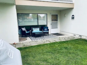 Un patio techado con mobiliario exterior, un cartel de bienvenida y una pequeña decoración que parece una casa en la pared.