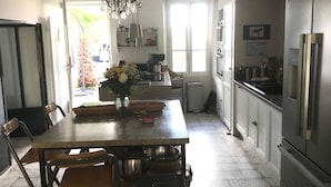 A kitchen with a dining table, chairs, a chandelier, cabinets, and a refrigerator. - Ile de re family house, garden swimming pool, close to the sea on foot. (Sainte-Marie-de-Ré)