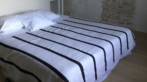 A bed with white bedding and black stripes, a lamp, a wardrobe, and a stone wall. - Ile de re family house, garden swimming pool, close to the sea on foot. (Sainte-Marie-de-Ré)