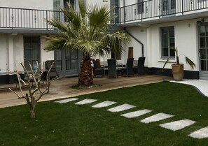 A courtyard with a palm tree, outdoor seating, and a white building with balconies. - Ile de Re Family Home, Garden, Pool, Within Walking Distance of the Ocean. (Sainte-Marie-de-Ré)