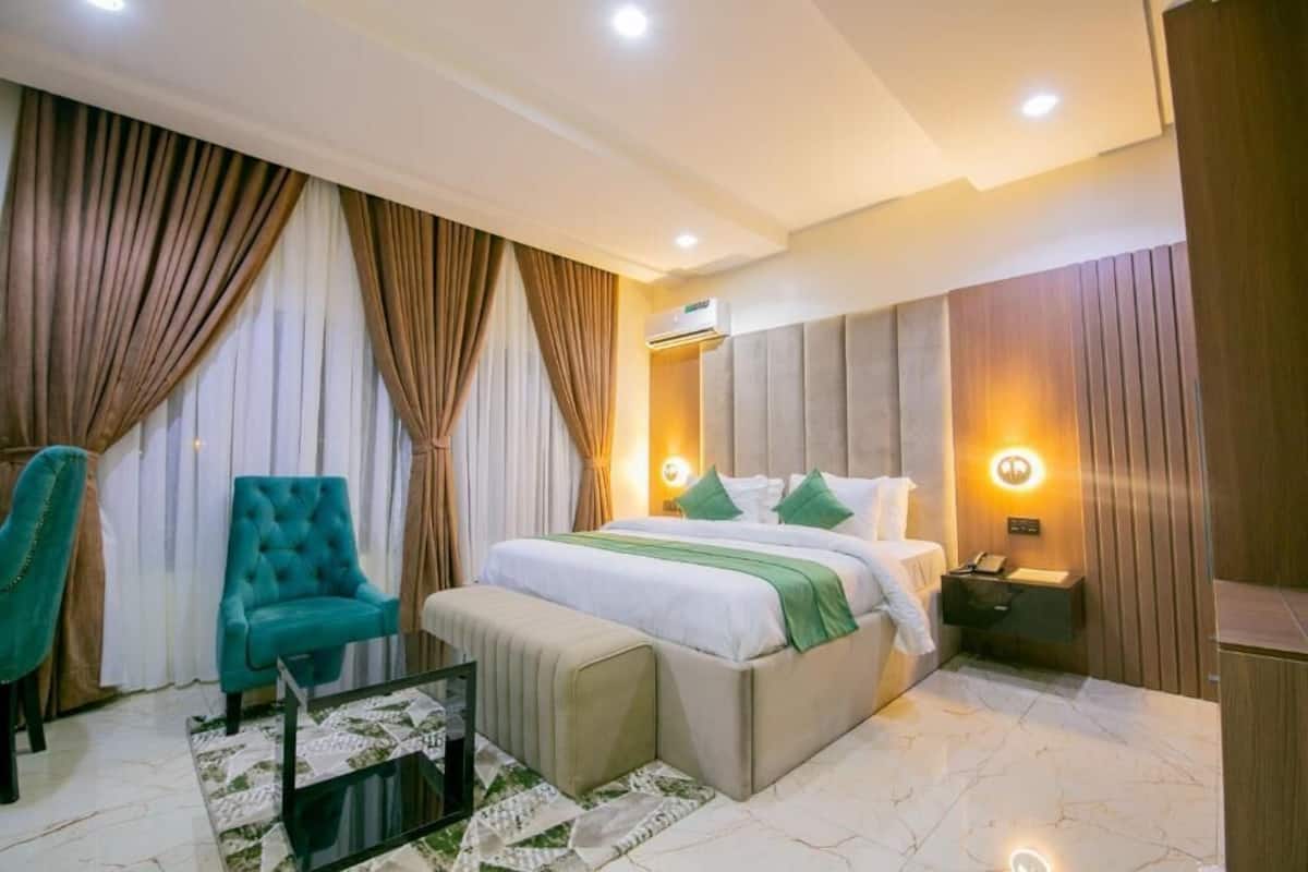 A bedroom with a bed, a chair, a bedside table, and an air conditioning unit.