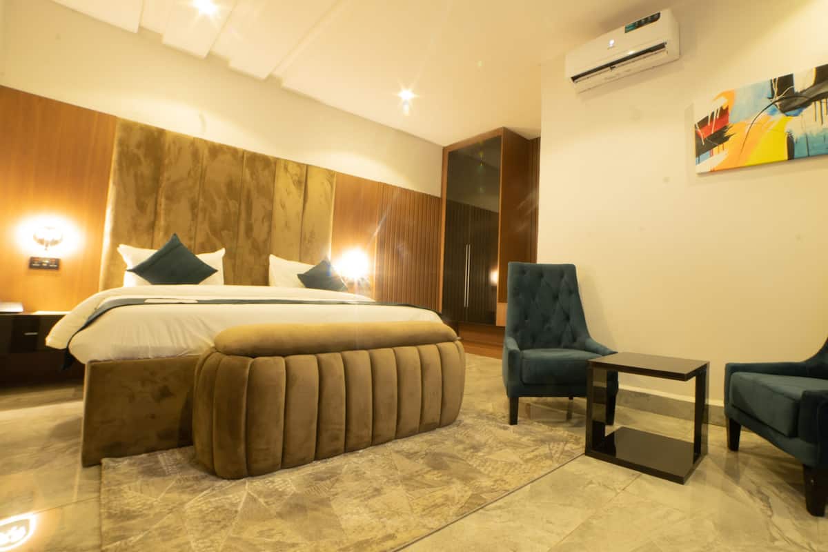 A modern hotel room with a large bed, two armchairs, a small table, and a painting on the wall.