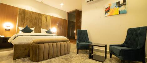 A modern hotel room with a large bed, two armchairs, a small table, and a painting on the wall.