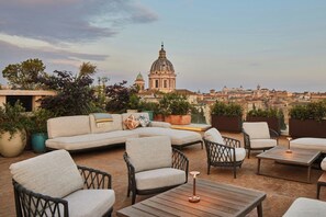 A rooftop terrace with outdoor seating, potted plants, and a view of a historic building. - Bvlgari Hotel Roma (Rome)